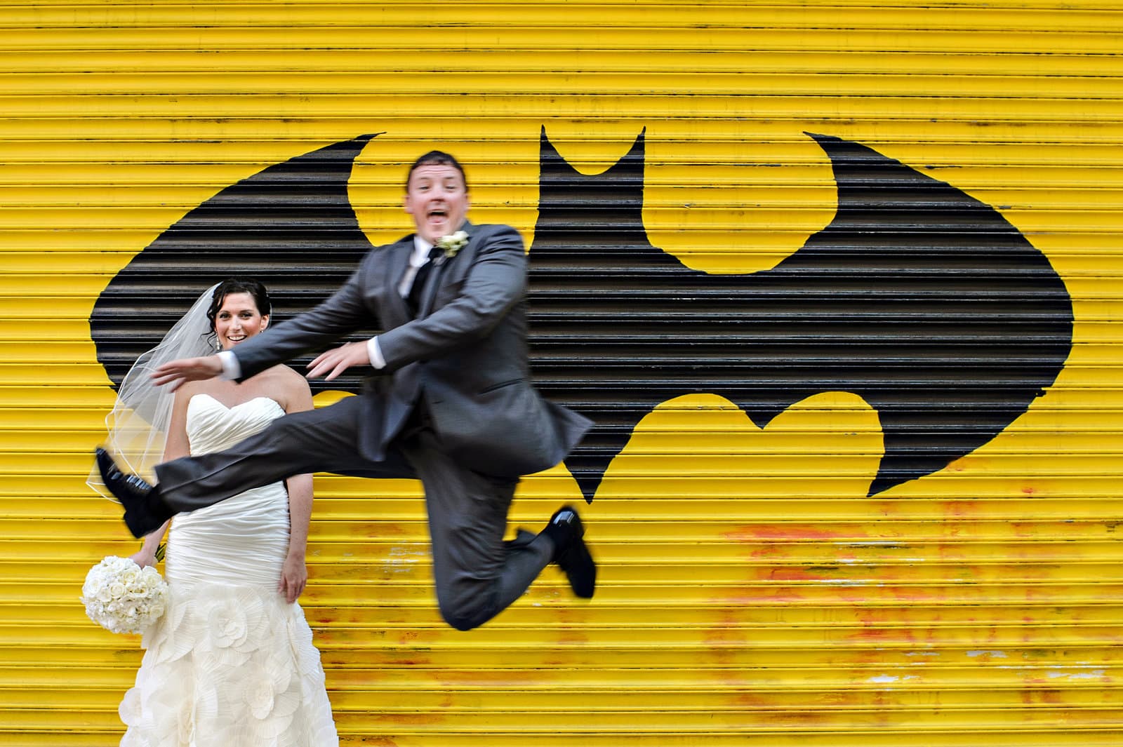 A groom leaping mid-air in front of a Batman mural